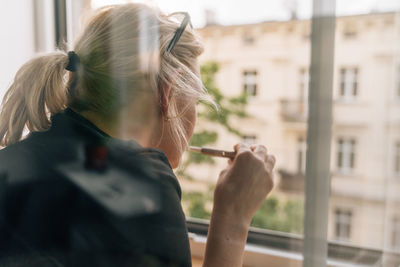 Side view of young woman looking through window