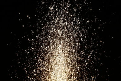 Low angle view of firework display over water against black background