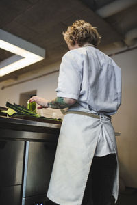 Rear view of female chef preparing kale at counter in kitchen