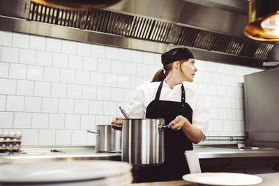 Female chef looking away while holding container in commercial kitchen