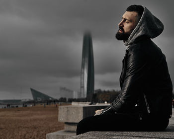 Side view of young man looking at city against sky