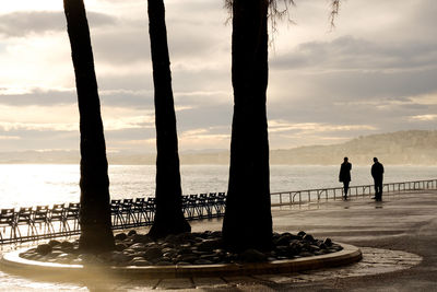 Silhouette people standing on beach against sky during sunset