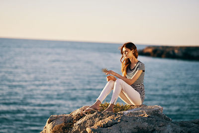 Woman sitting on rock by sea against sky