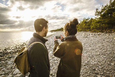 Man looking at woman photographing sea against sky from mobile phone at beach