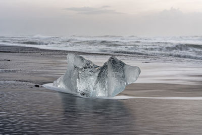 Striking block of ice on a black beach with surf, with returning water reflection on the wet sand