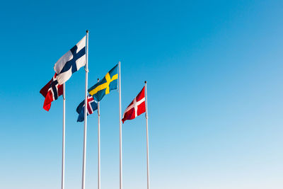 Low angle view of flags against clear blue sky