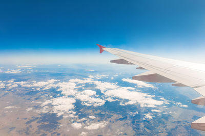 Aerial view of airplane flying over clouds against blue sky