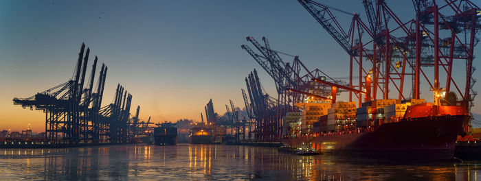 Cranes at commercial dock against sky during sunset