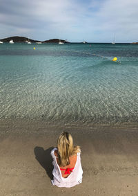 Rear view of woman sitting on beach against sky