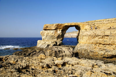 Stone wall by sea against clear blue sky