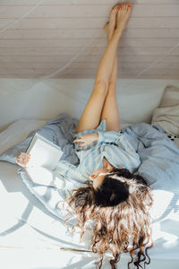 High angle view of young woman reading book while lying on bed at home