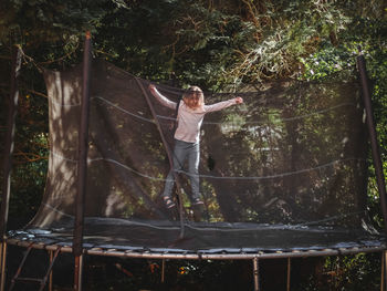 A beautiful caucasian girl in jeans and a t-shirt with sleeves jumps on a trampoline