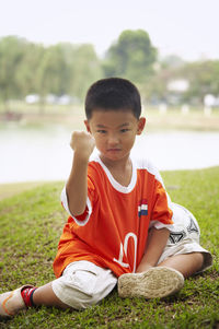 Full length portrait of confident boy with soccer ball gesturing on field at park