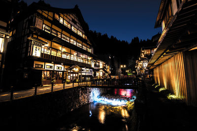 Illuminated bridge over canal amidst buildings in city at night