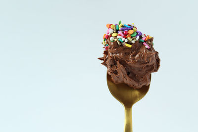 Close-up of chocolate with sprinklers on spoon against white background