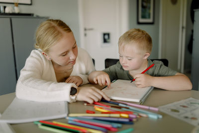 Girl assisting brother with down syndrome in drawing on book at home