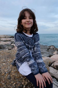 Portrait of smiling girl sitting on rock at beach 