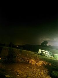 Illuminated street amidst field against sky at night