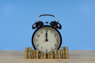 Close-up of alarm clock and coins on table against blue background