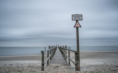 Wooden pier over beach against cloudy sky