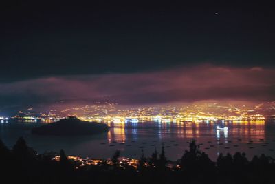 High angle view of illuminated city by sea against sky at night