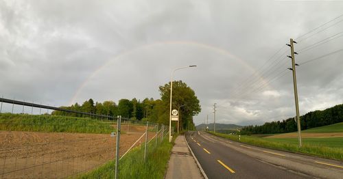 Rainbow over road amidst field against sky