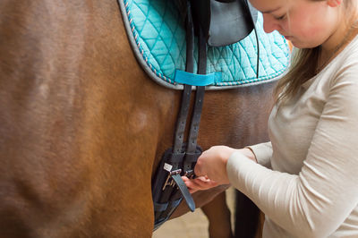 Woman fastening saddle belt on horse