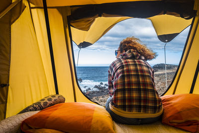 Rear view of mature woman sitting in tent at beach