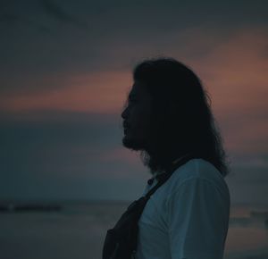 Side view of woman looking away against sky during sunset