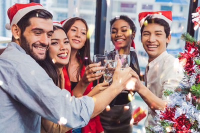 Portrait of cheerful friends toasting drinks during christmas