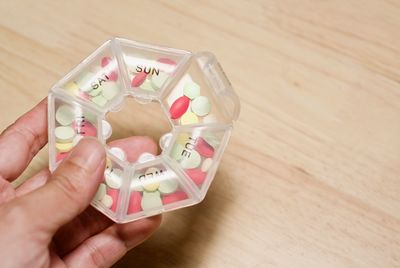 Cropped hand holding pills in container on table