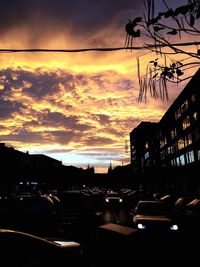 Cars on street amidst silhouette buildings against sky during sunset