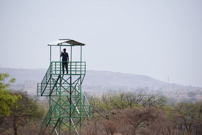 Low angle view of man standing on lookout tower against clear sky