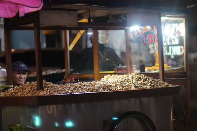 Male vendor selling peanuts at market stall during night