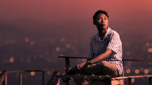 Young man looking away while standing against railing