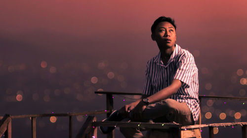 Young man looking away while sitting against railing