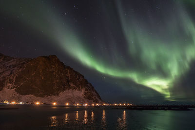 Aurora borealis over lake and mountain against star field at night during winter