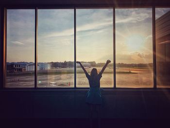 Rear view of woman standing by window against sky