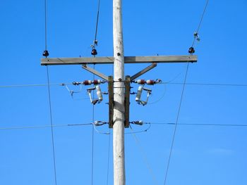 Low angle view of electricity pylon against clear blue sky