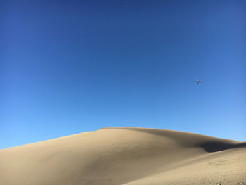 Low angle view of airplane flying over desert against clear blue sky