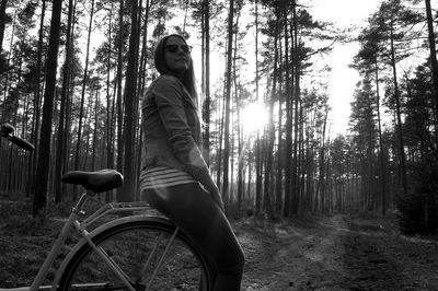 Woman sitting on bicycle against trees at forest