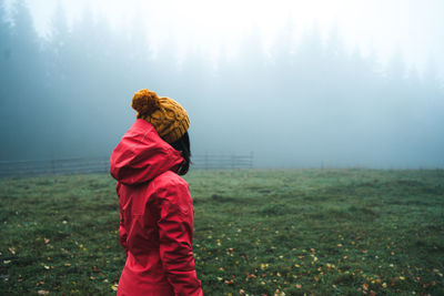 Rear view of woman standing on field during foggy weather