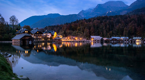 Scenic view of lake by illuminated buildings against sky at dusk