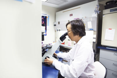 Side view of senior female scientist using microscope