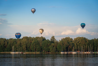 Hot air balloons flying over lake against sky