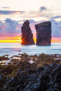 Rocks on sea shore against sky during sunset