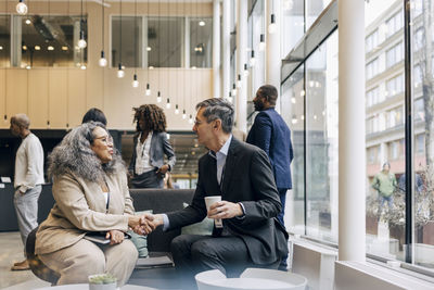 Businesswoman doing handshake with male entrepreneur while sitting on couch at convention center