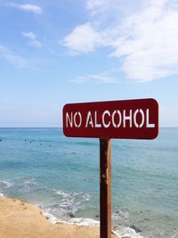 Close-up of information sign on beach against sky