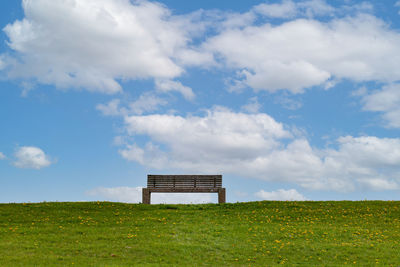 Empty bench on field against sky