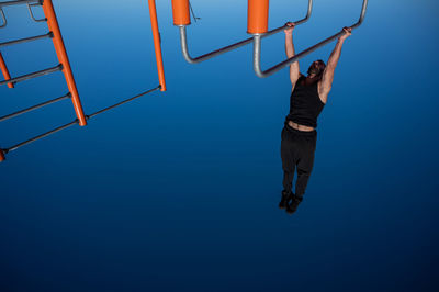 Shirtless man doing horizontal balance on parallel bars at sports ground. 